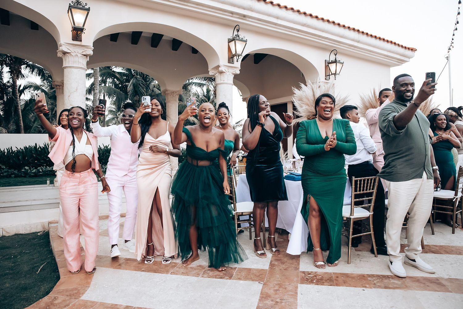 Wedding celebration with guests in coordinated green and pink attire at an outdoor venue.
