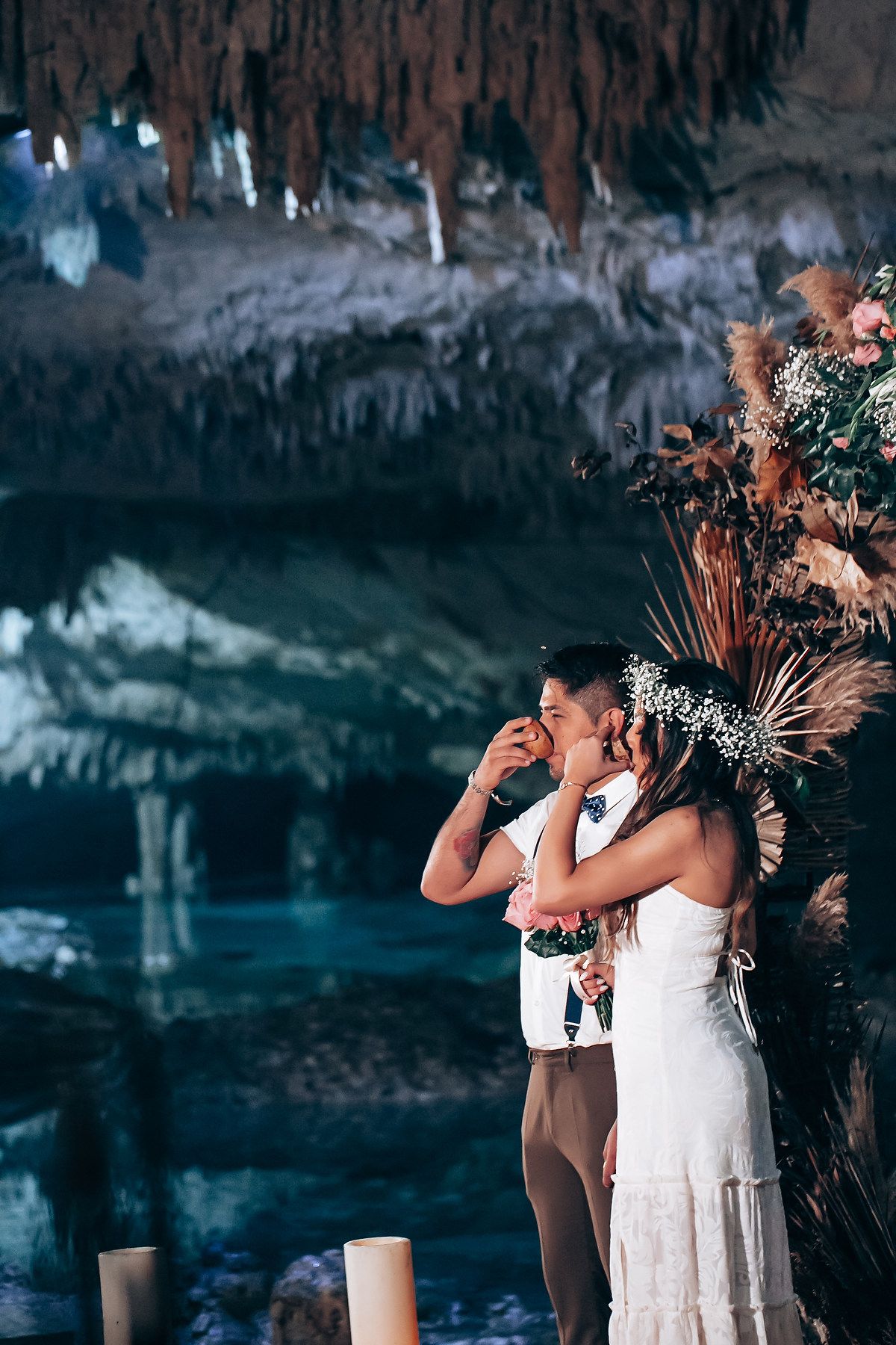 A wedding celebration sequence showing people in white attire taking shots of tequila in a rustic cave-like setting.