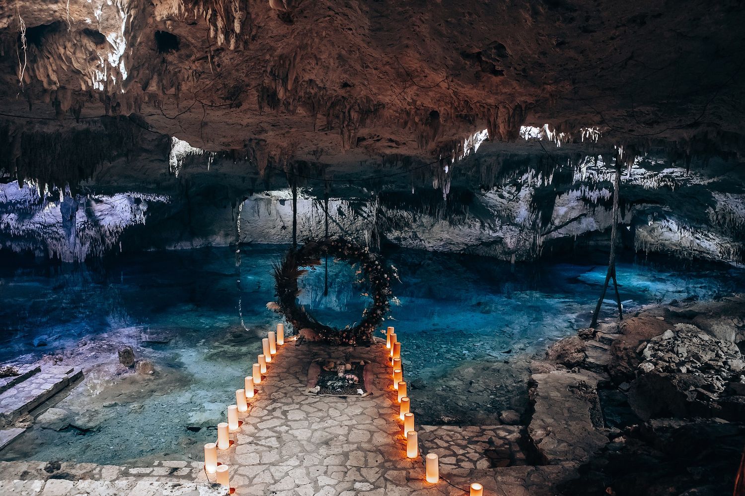 A series of illuminated paper lanterns create a mystical path through a dark cave with turquoise water.