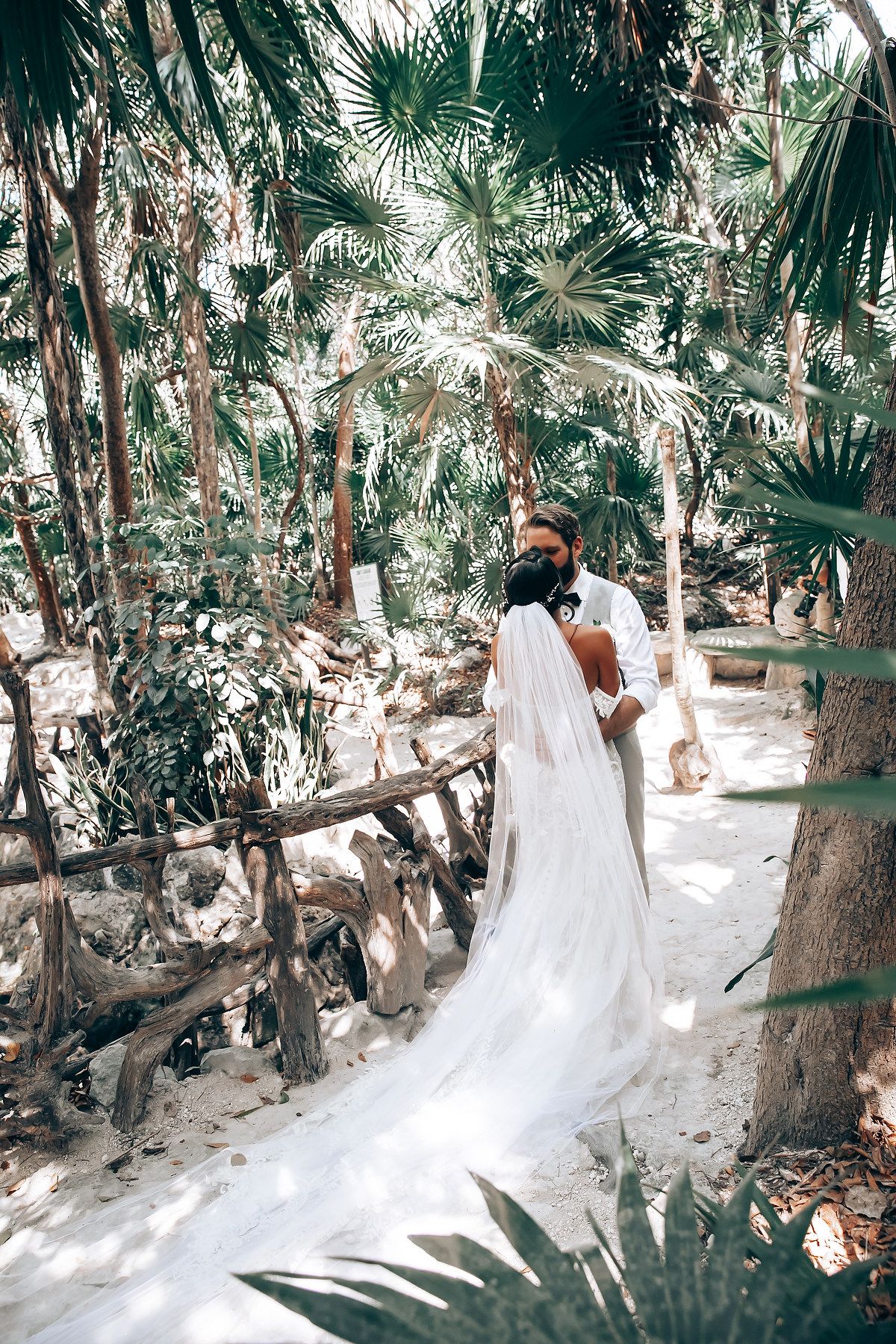 A white wedding dress train flows elegantly along a palm-lined sandy pathway.