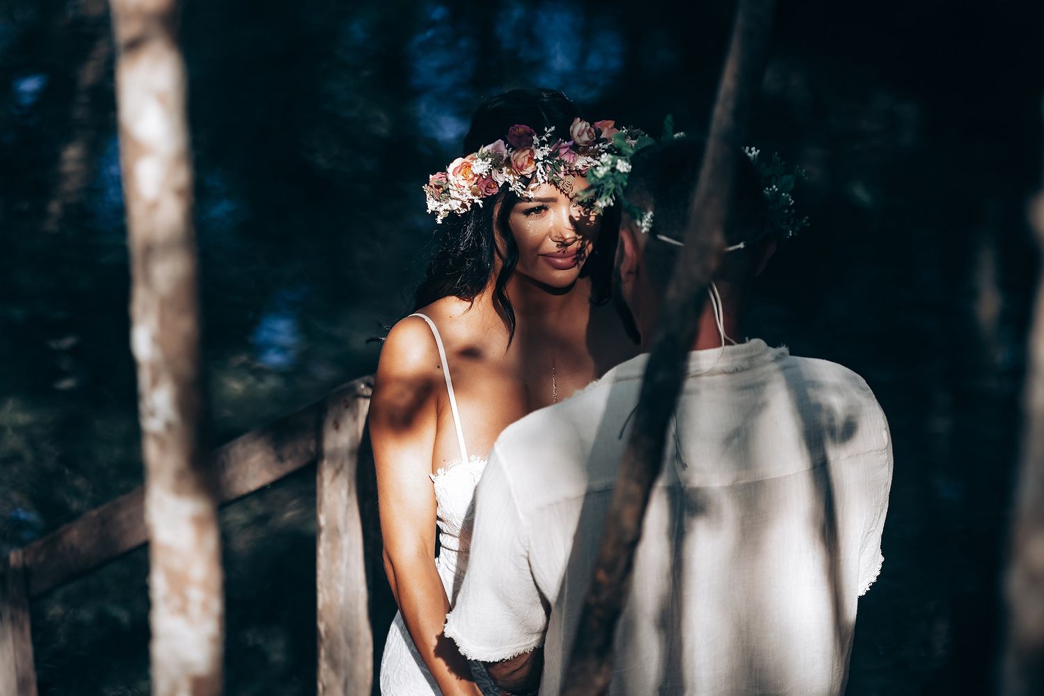 A person in a white dress poses in a dark moody forest setting with dramatic lighting and shadows.