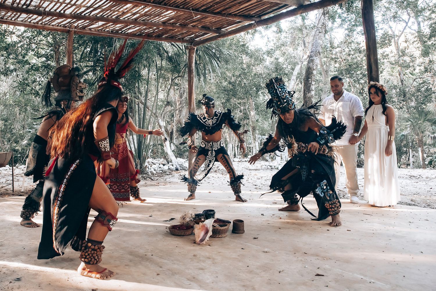 Traditional ceremony participants gather beneath a wooden canopy in a forest setting.