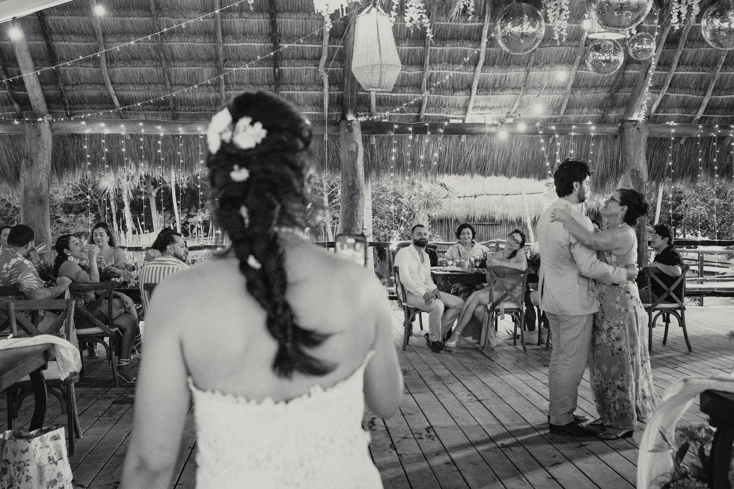 Black and white photo of bride and groom sharing first dance at outdoor wedding reception with string lights.