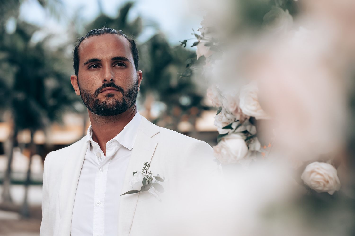 Wedding party members in white attire posing among tropical palm trees.