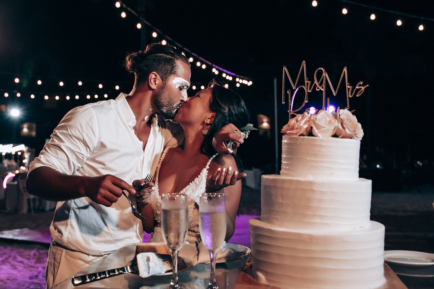 Wedding reception detail of string lights and white tiered cake at night.