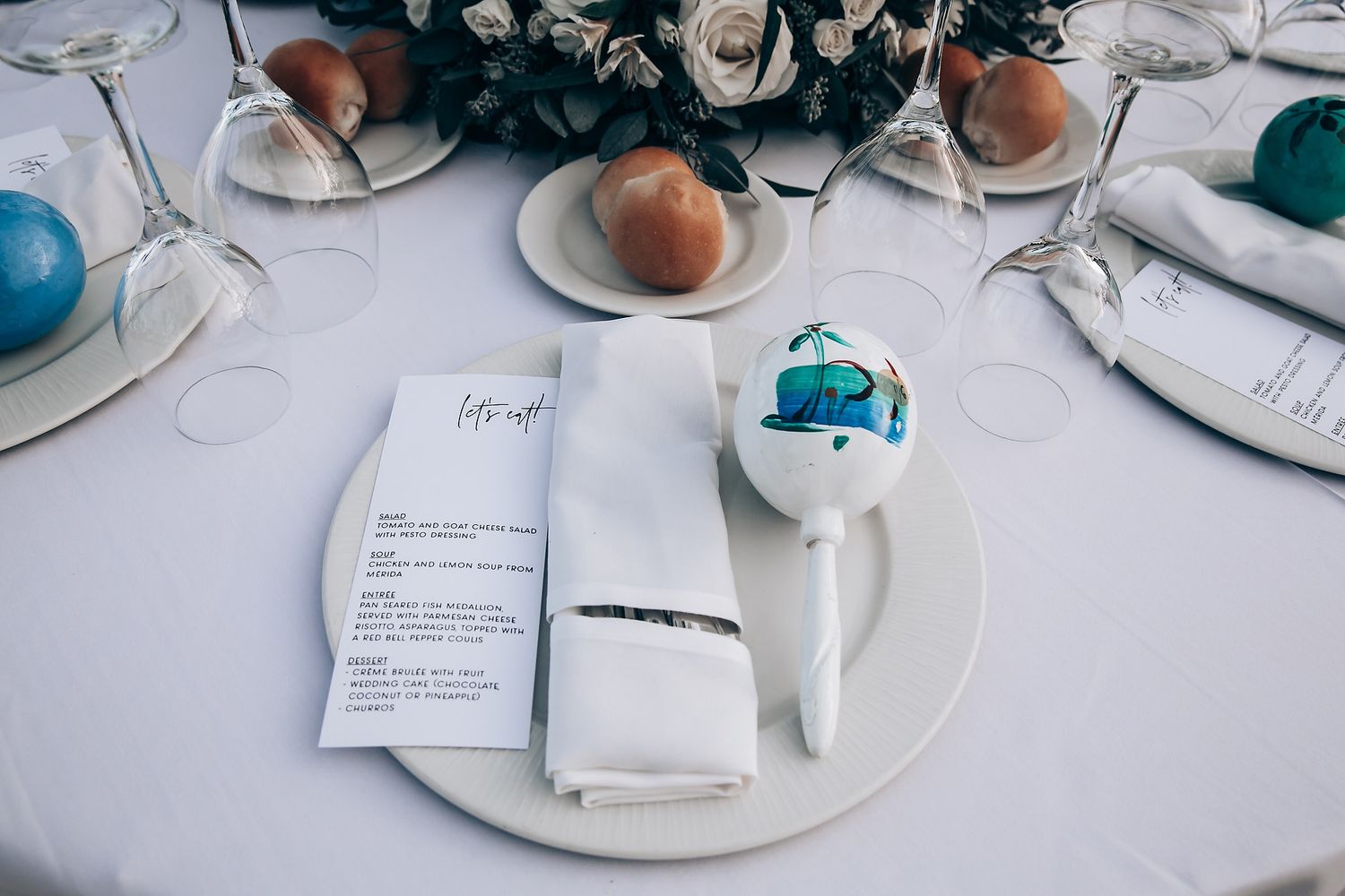 Wedding place setting with menu card, peach, and blue decorative elements on white tablecloth.