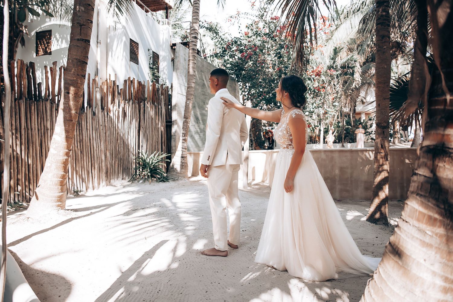 Sun-drenched wedding ceremony walkway lined with palm trees and white-clad guests.