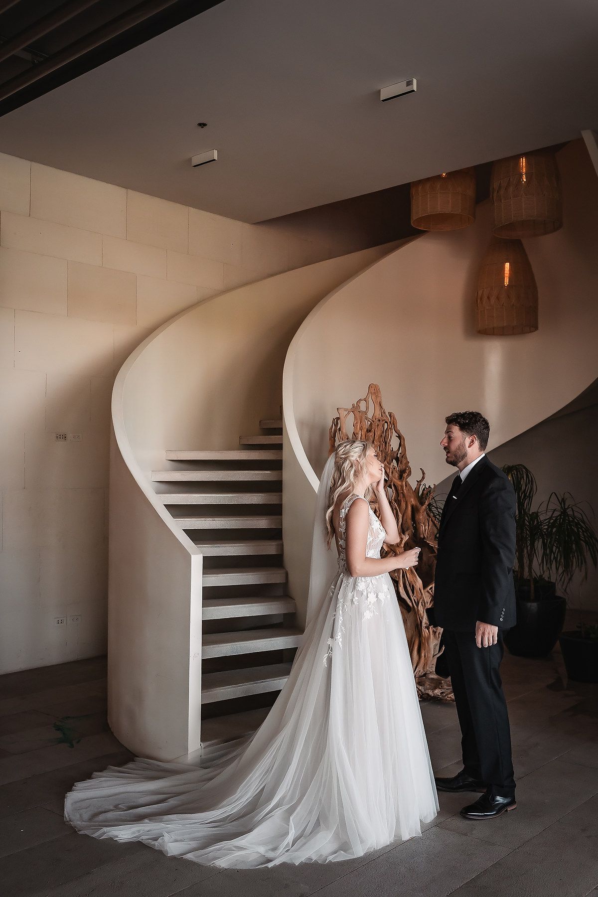 First look wedding moment captured in sequence under curved staircase with dramatic lighting.