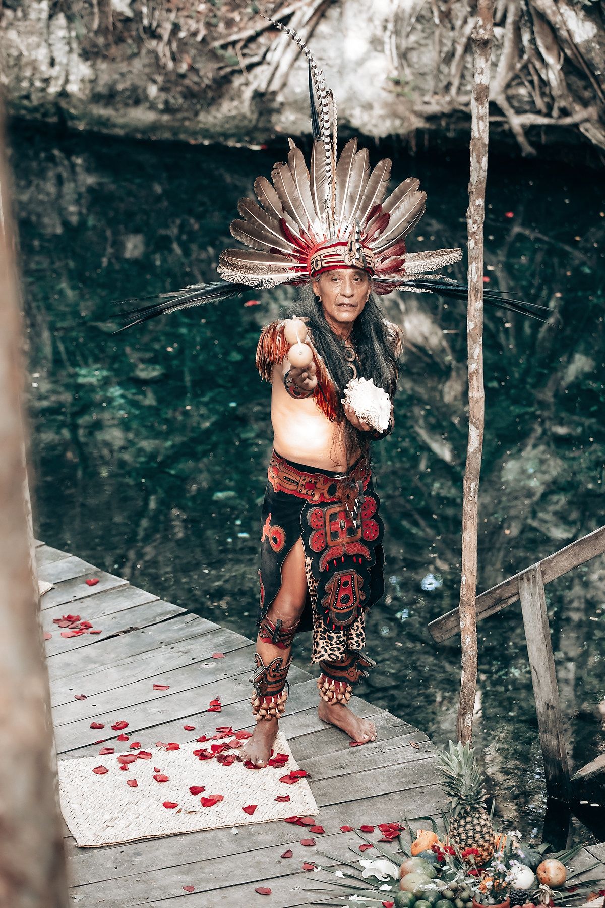 Performers in traditional indigenous regalia on a wooden platform with rose petals.