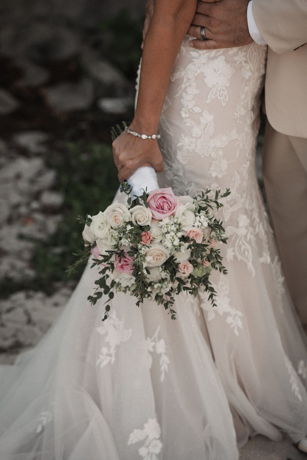 Close-up of bride holding romantic pink and white rose bouquet in lace mermaid wedding dress.