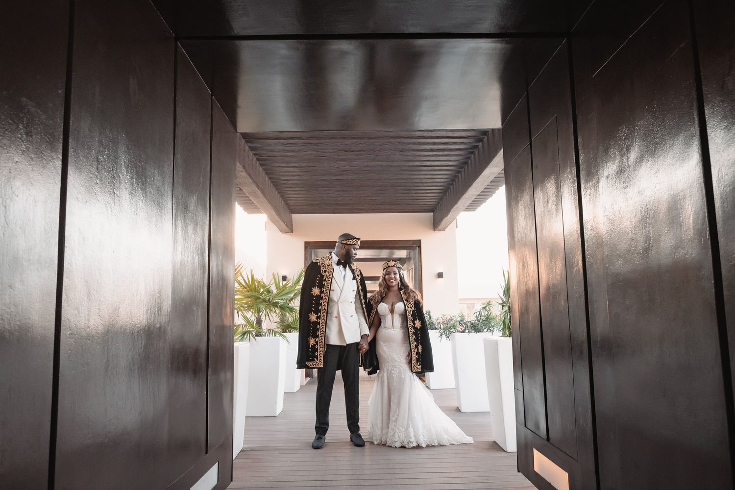 Bride and groom pose together in a dramatic hallway framed by dark wooden doors.
