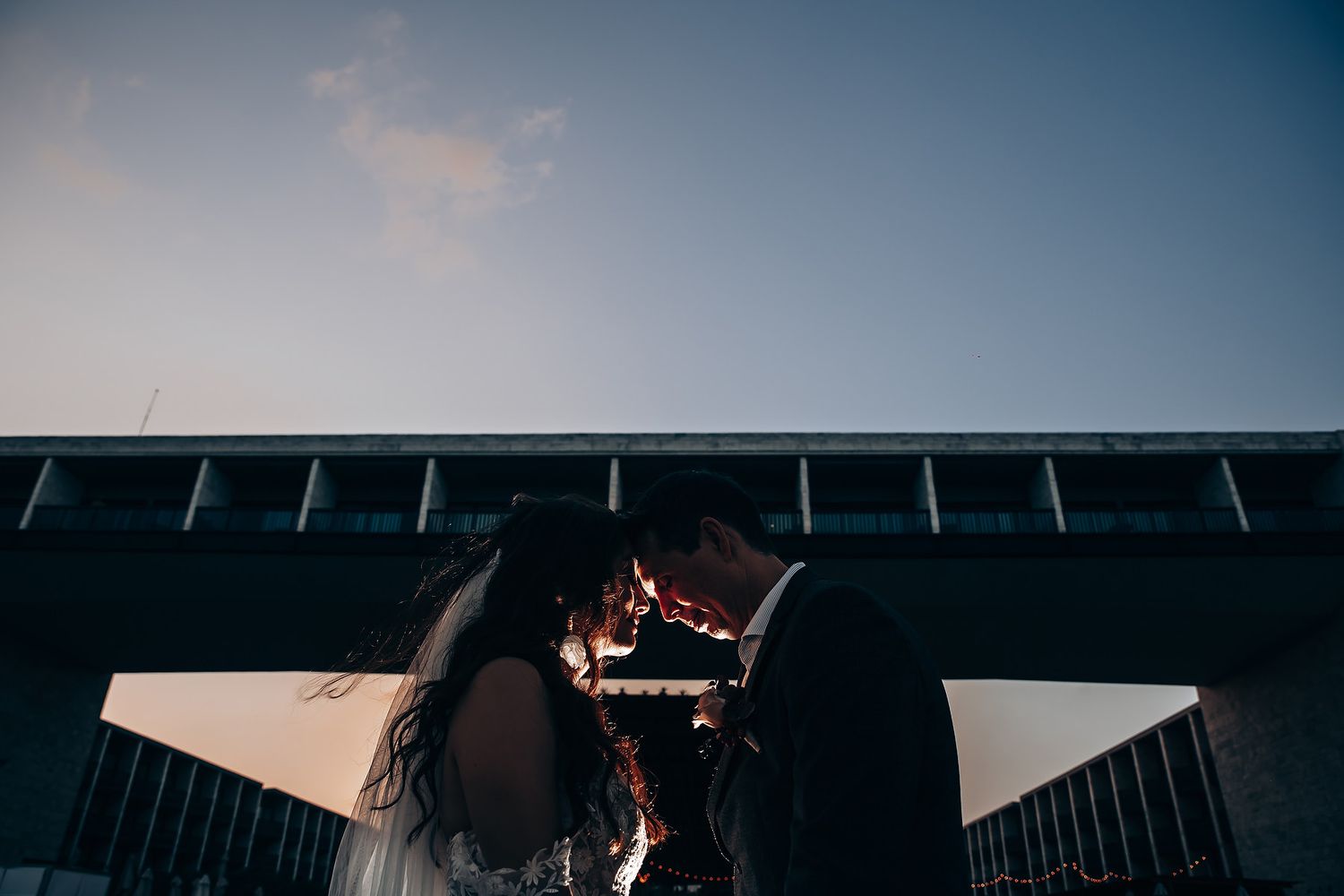 Silhouetted romantic moment against modern architectural backdrop at dusk.