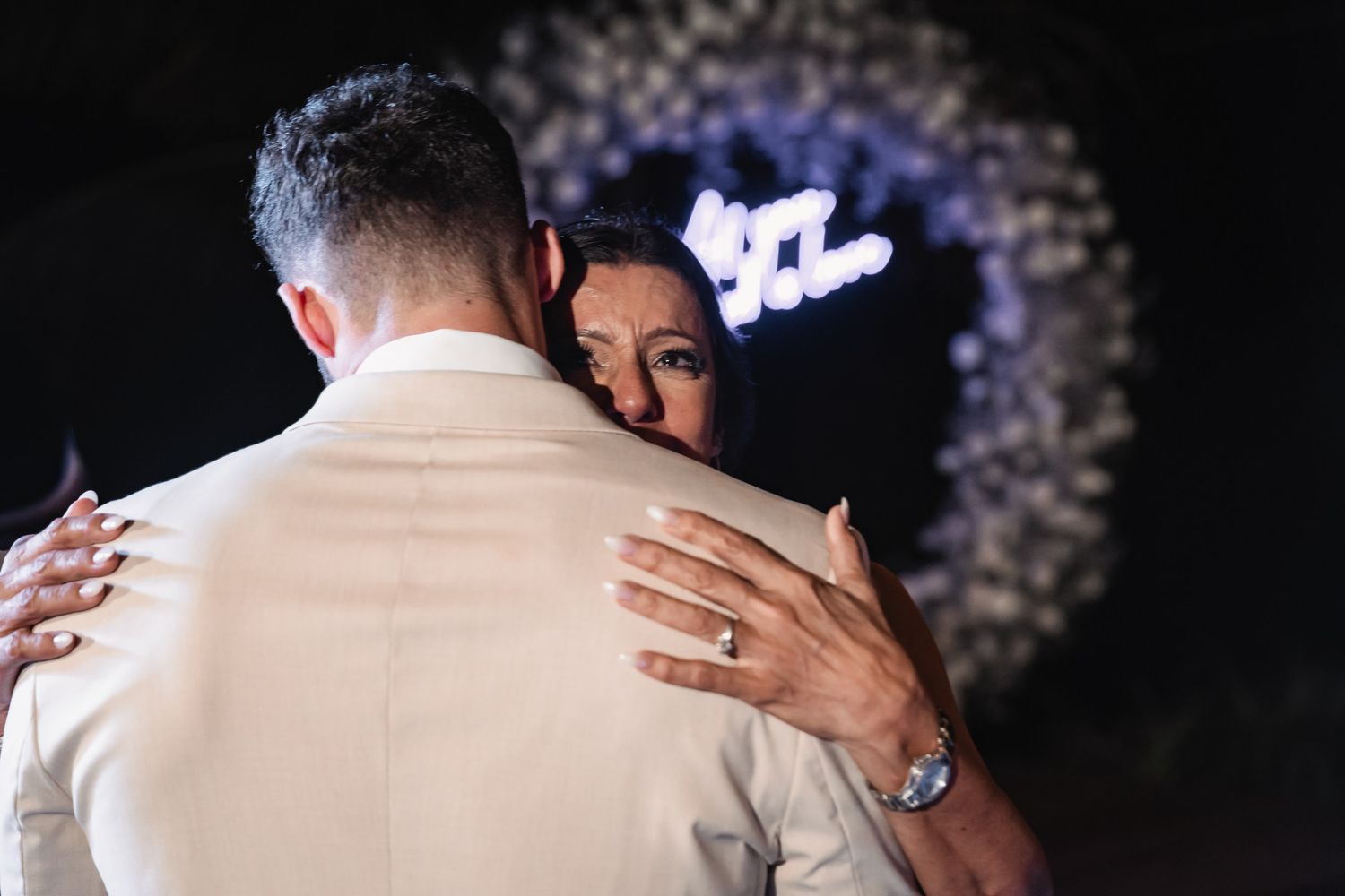 Couple sharing an emotional first dance embrace with a glowing neon heart sign in the background.