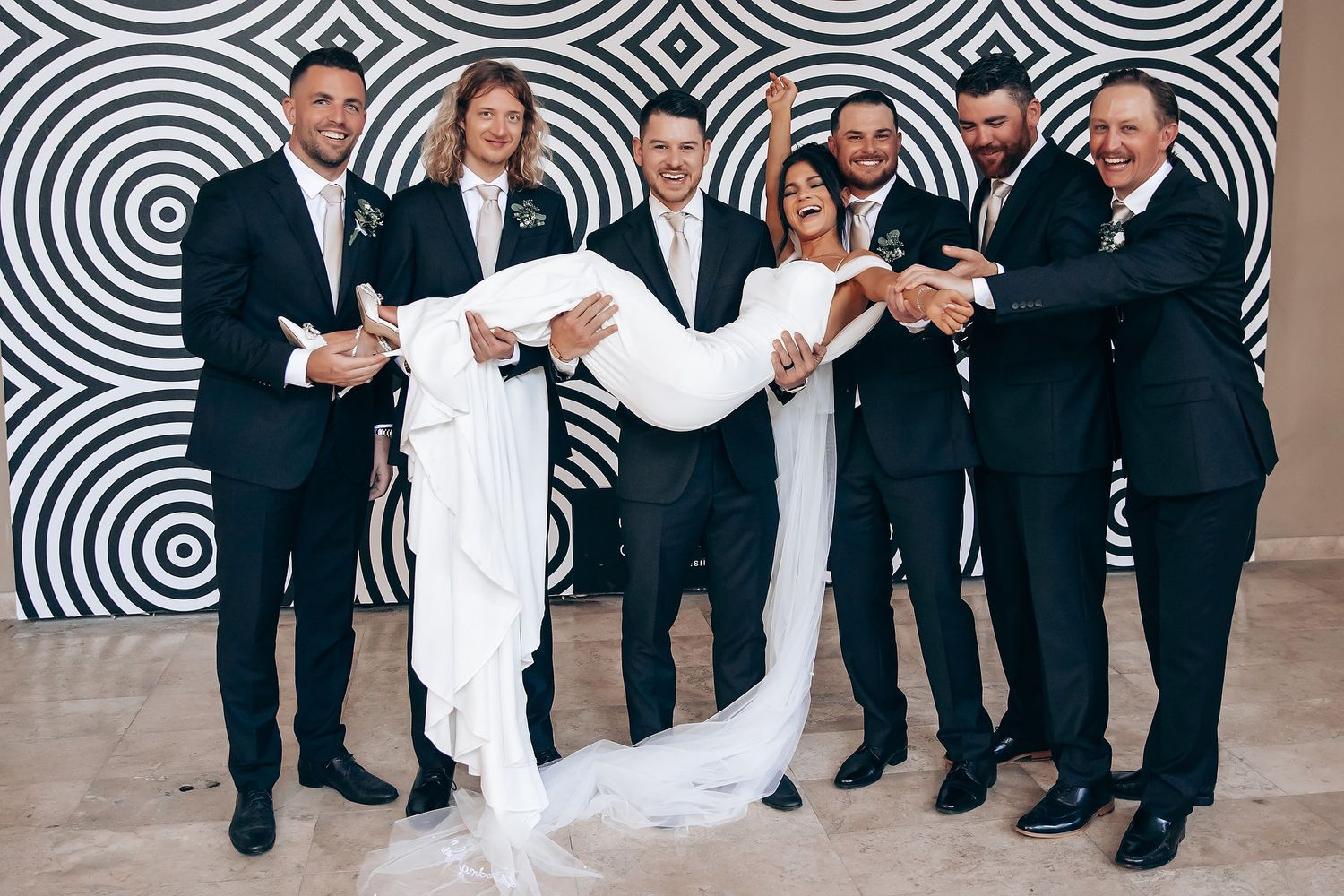 Wedding party poses against geometric black and white patterned wall during formal photos.