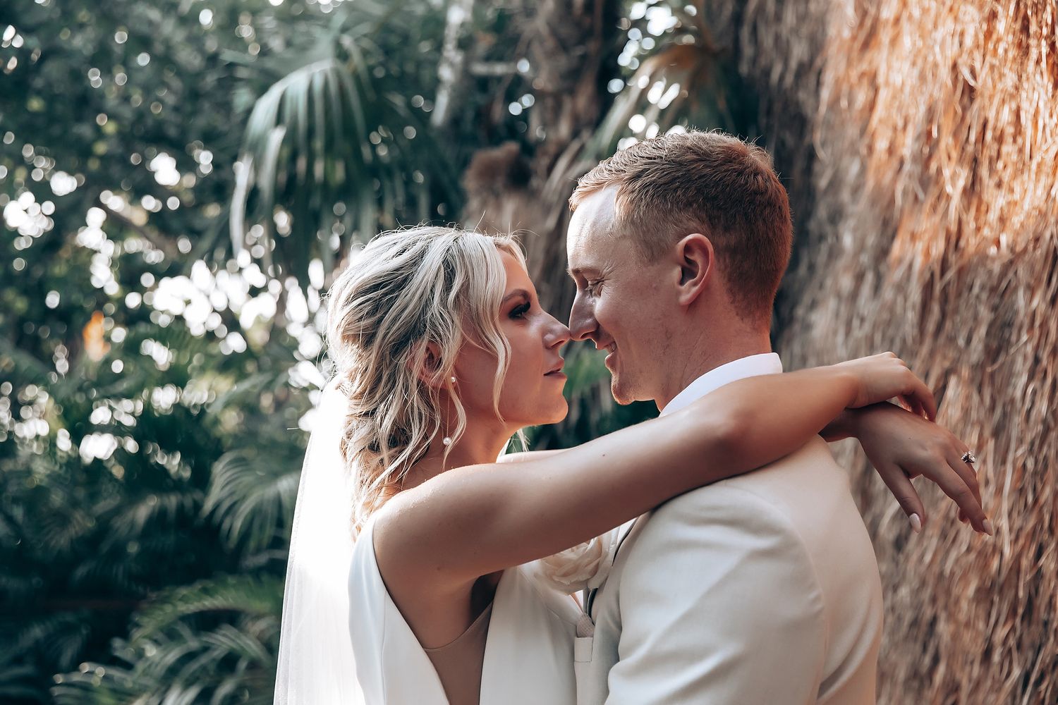 Romantic wedding couple shares intimate moments under palm trees during sunset.
