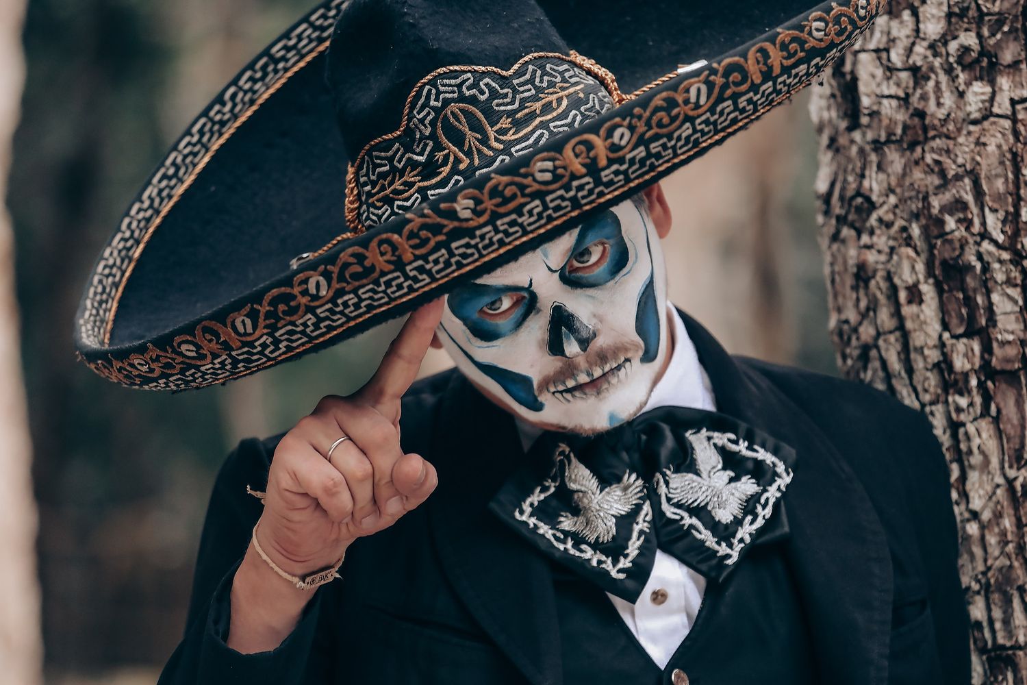A person in a decorative black sombrero and formal attire poses against a textured background.