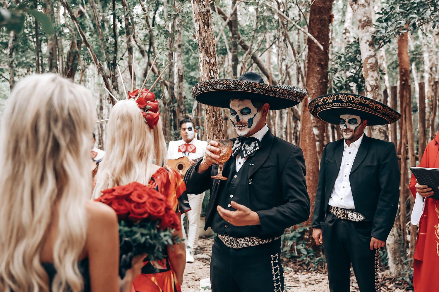 Couple in Halloween costumes dancing in a forest setting with guests watching in the background.