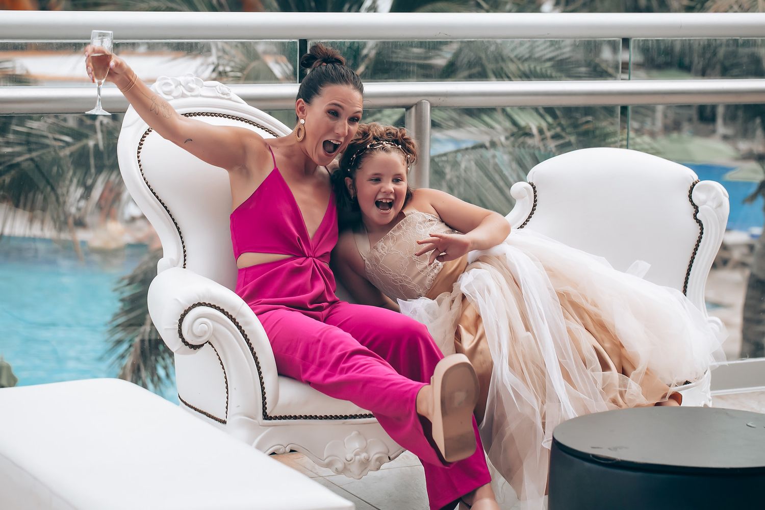 Two people sharing a joyful moment while sitting on an elegant white couch by a pool.
