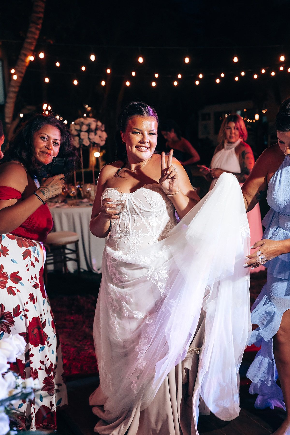 Evening wedding reception with string lights and guests dancing in festive attire.