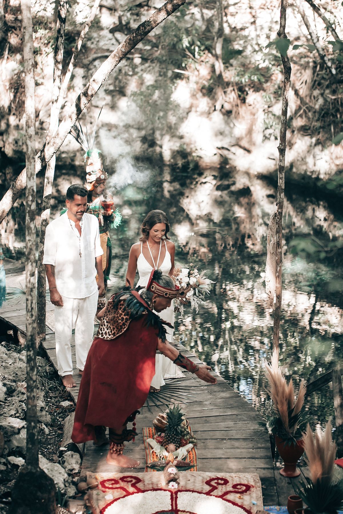 A couple walks along a wooden bridge in a lush, tropical forest setting.