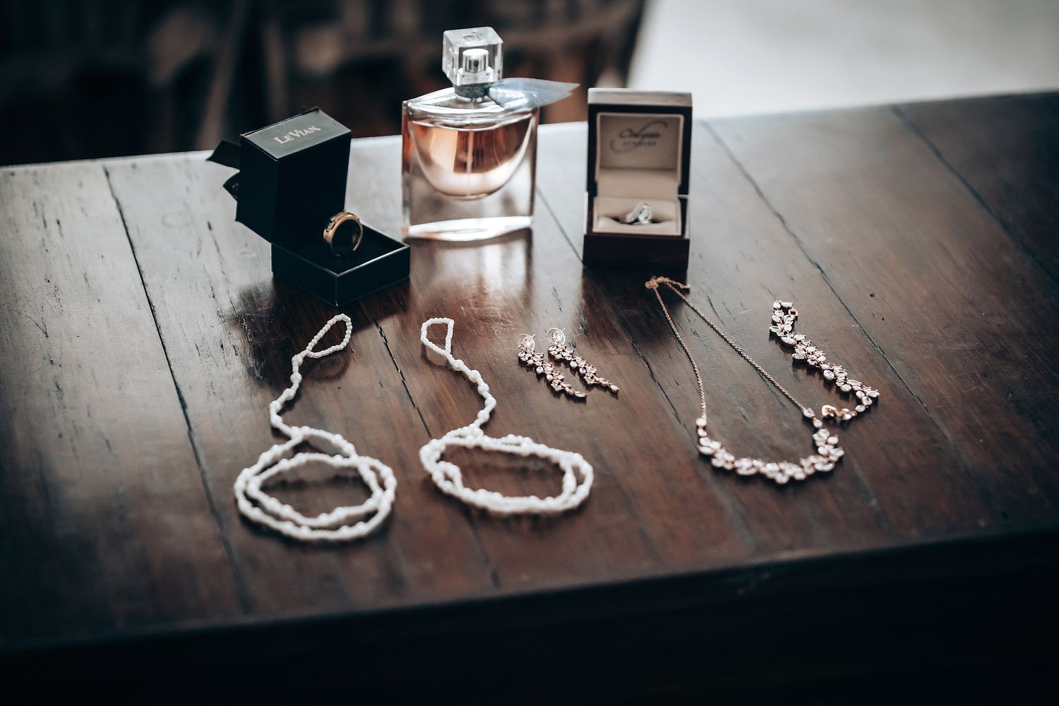 A collection of jewelry, including a perfume bottle, necklaces, and rings, displayed on a wooden surface.