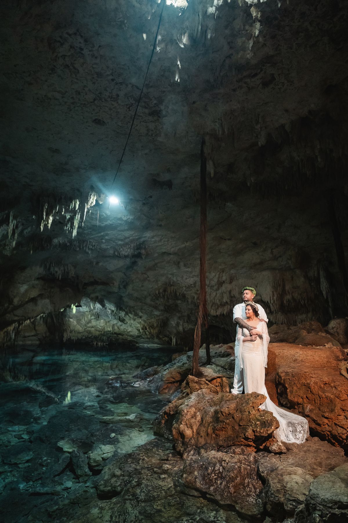 A couple poses for wedding photos in a dramatic underground cave setting with atmospheric lighting.