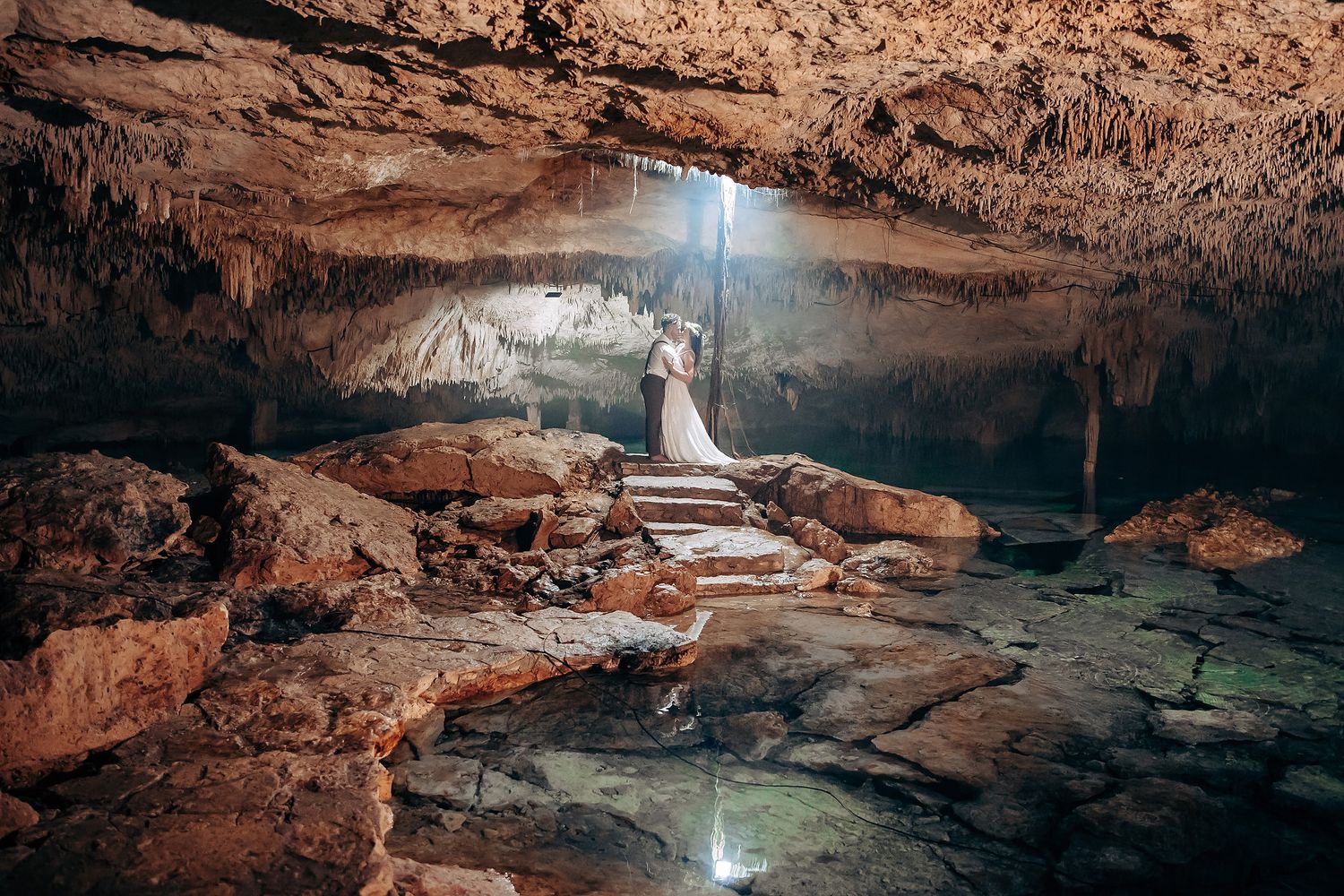 Natural light streams into a limestone cave during a wedding ceremony, illuminating the rocky cavern walls.