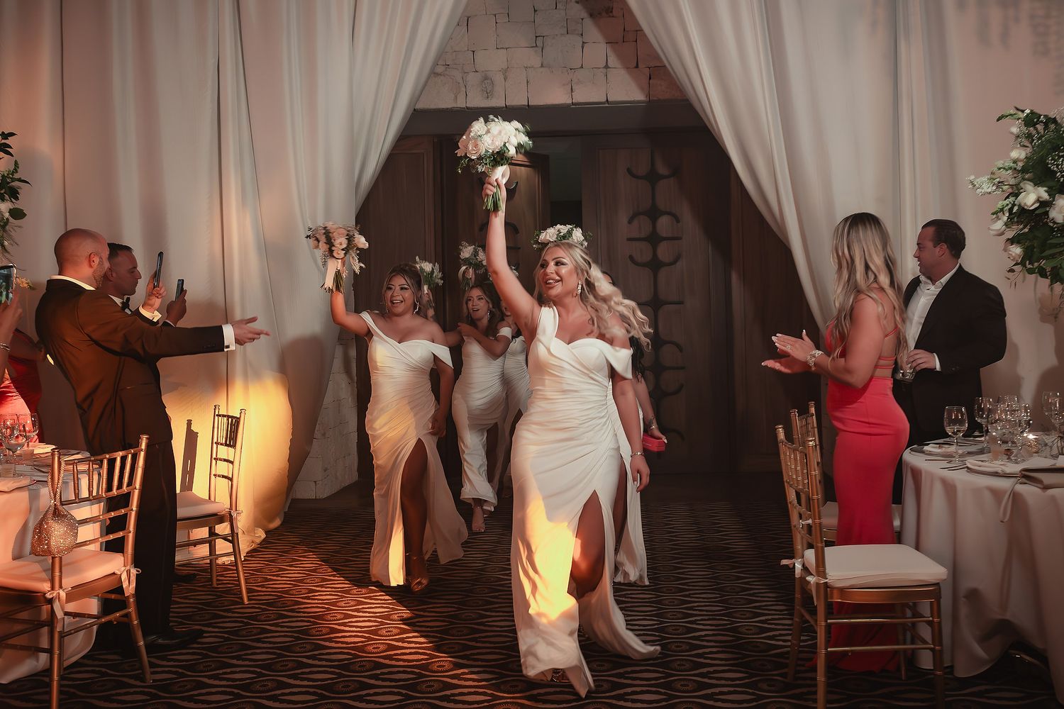 Wedding guests dance and celebrate together on a dimly lit dance floor at an indoor reception venue.