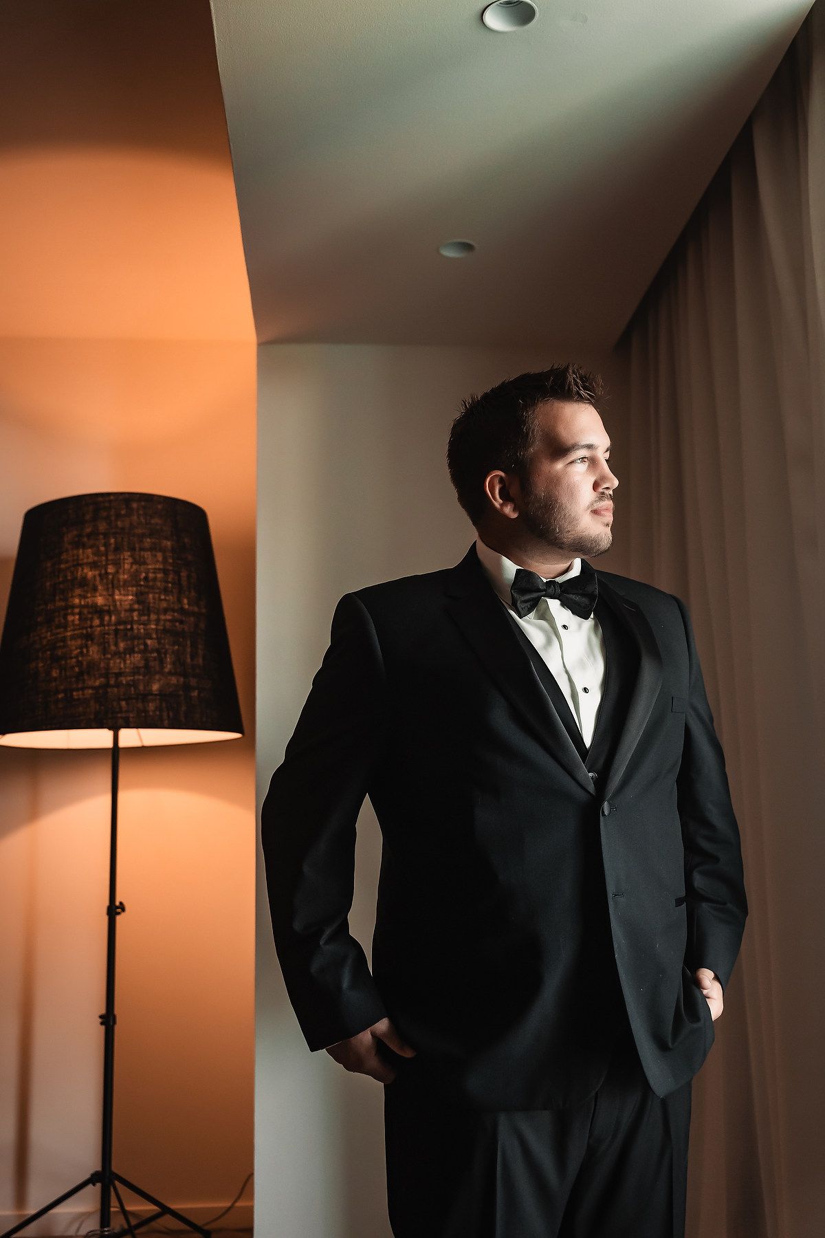 Moody portrait sequence of someone in a black tuxedo standing near a tall floor lamp with dramatic lighting.