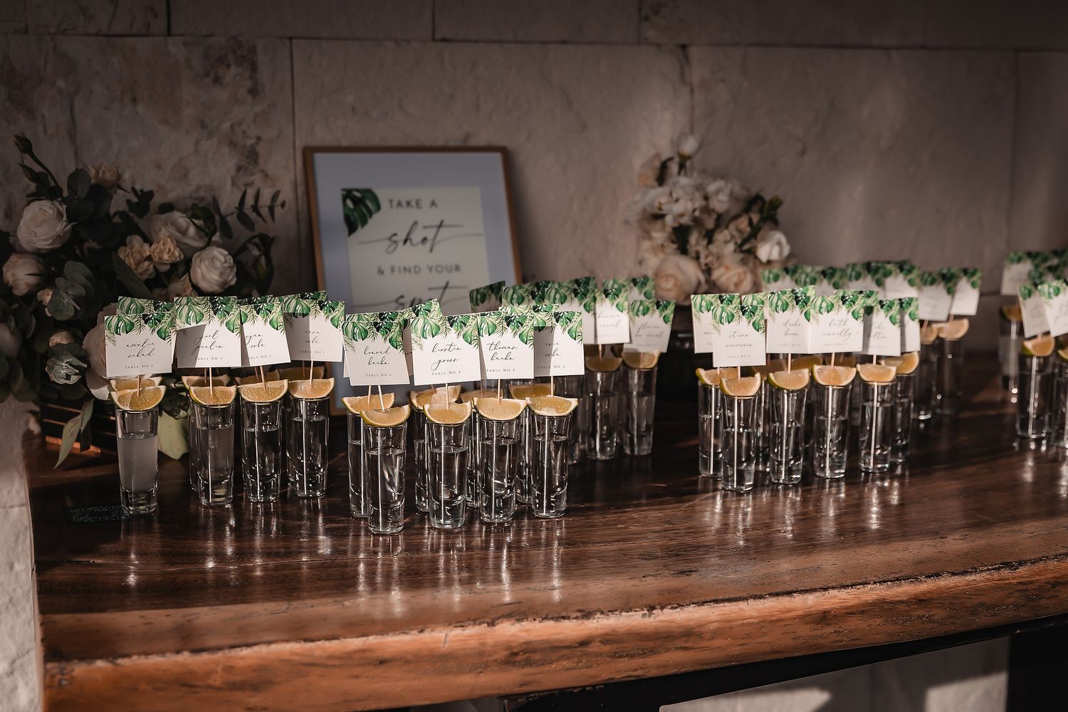 Row of elegant glass vases with floral arrangements and name cards displayed on wooden table.