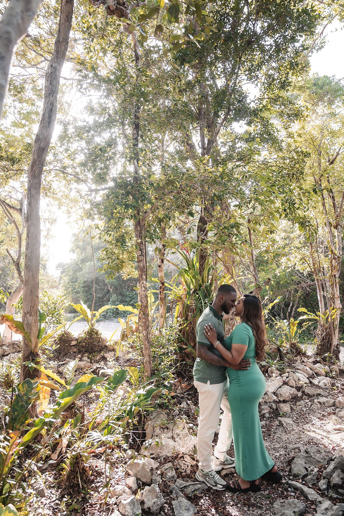 A romantic couple shares tender moments in a wooded area with natural stone formations.