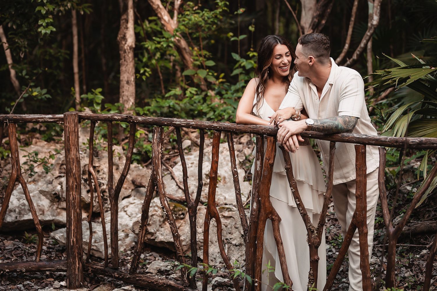 Two people share an intimate moment along a wooden railing in a tropical setting.