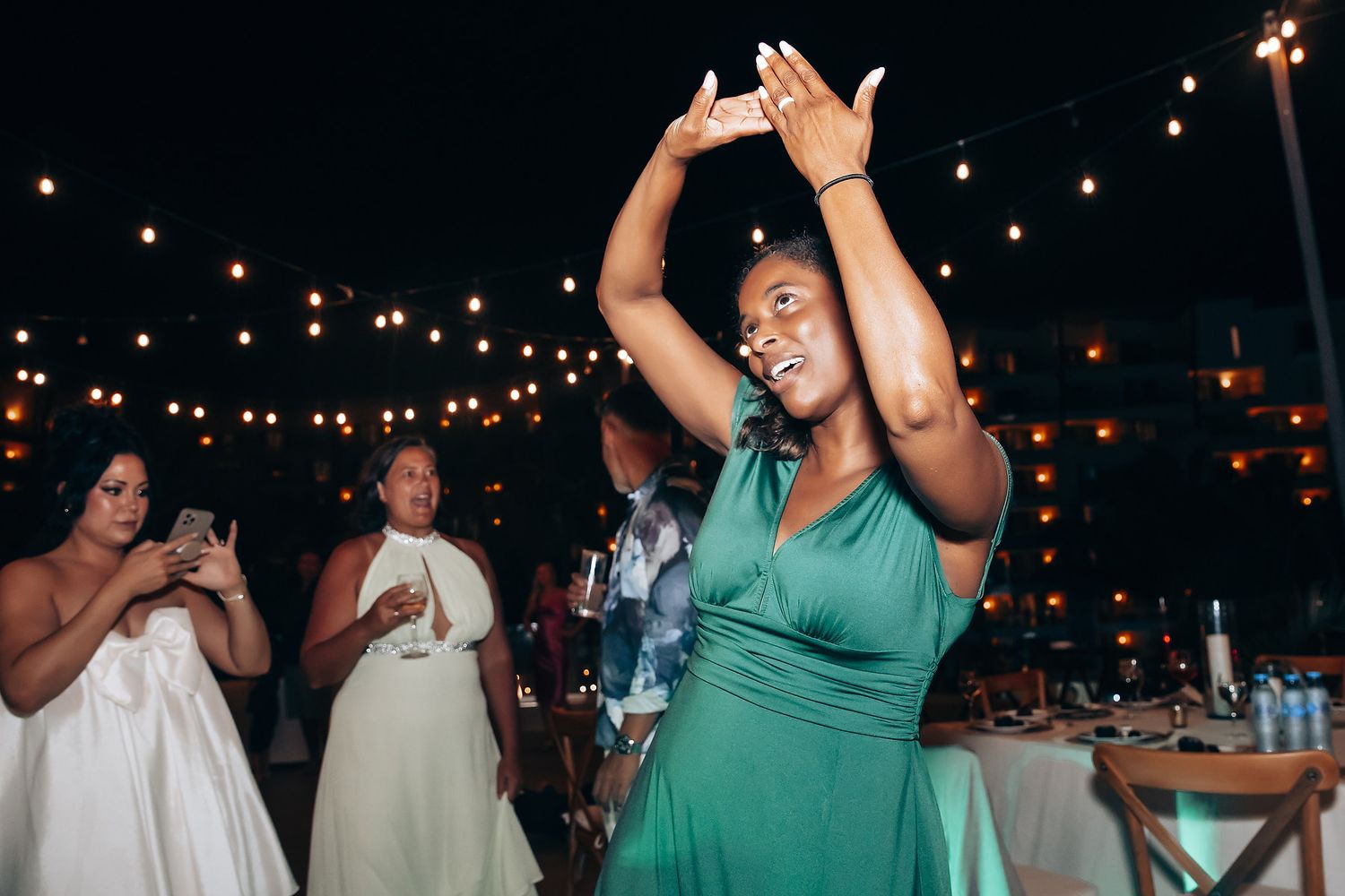 Wedding guests dancing and celebrating under string lights at an outdoor reception.