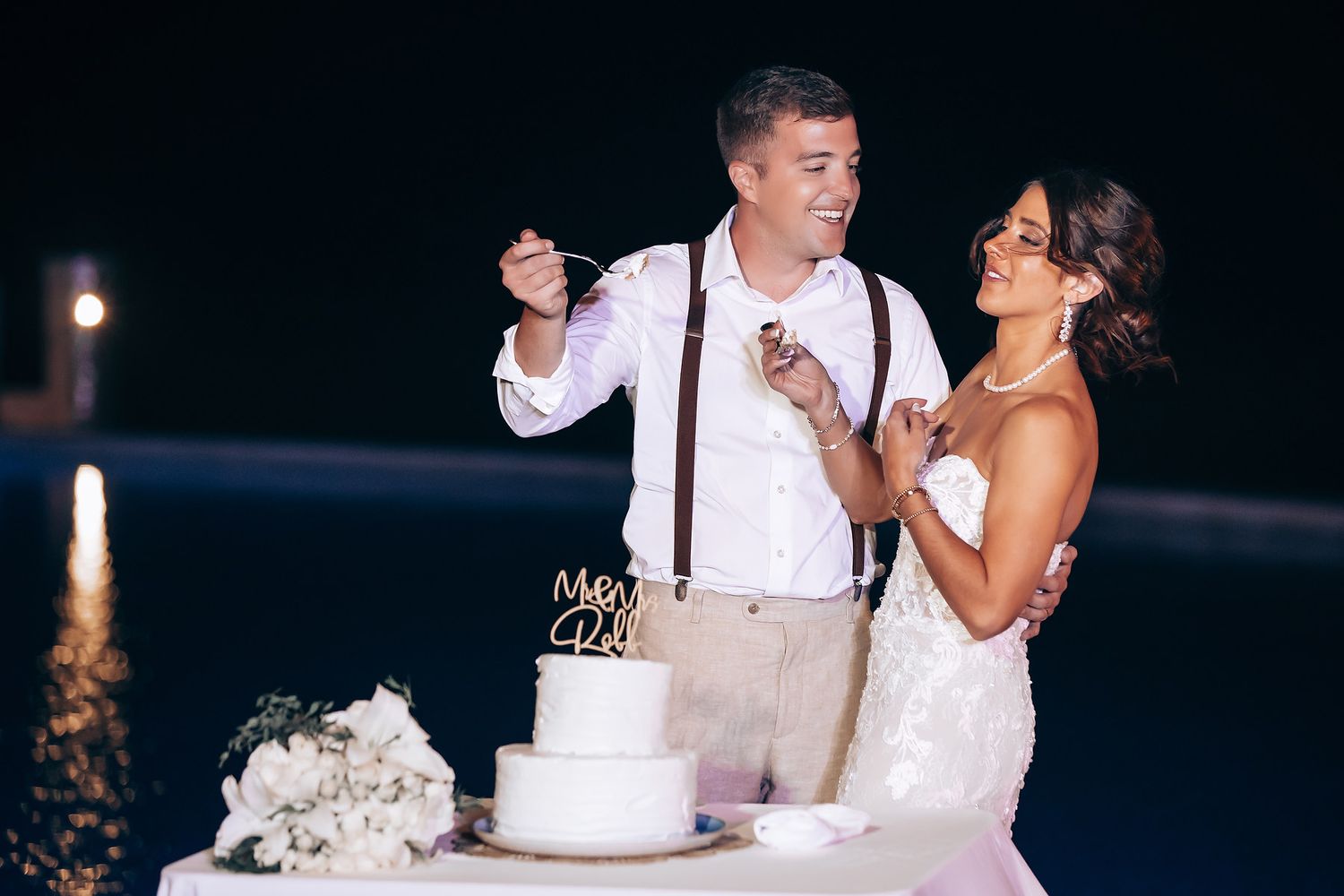 Wedding couple cuts their elegant white wedding cake together at their evening reception.