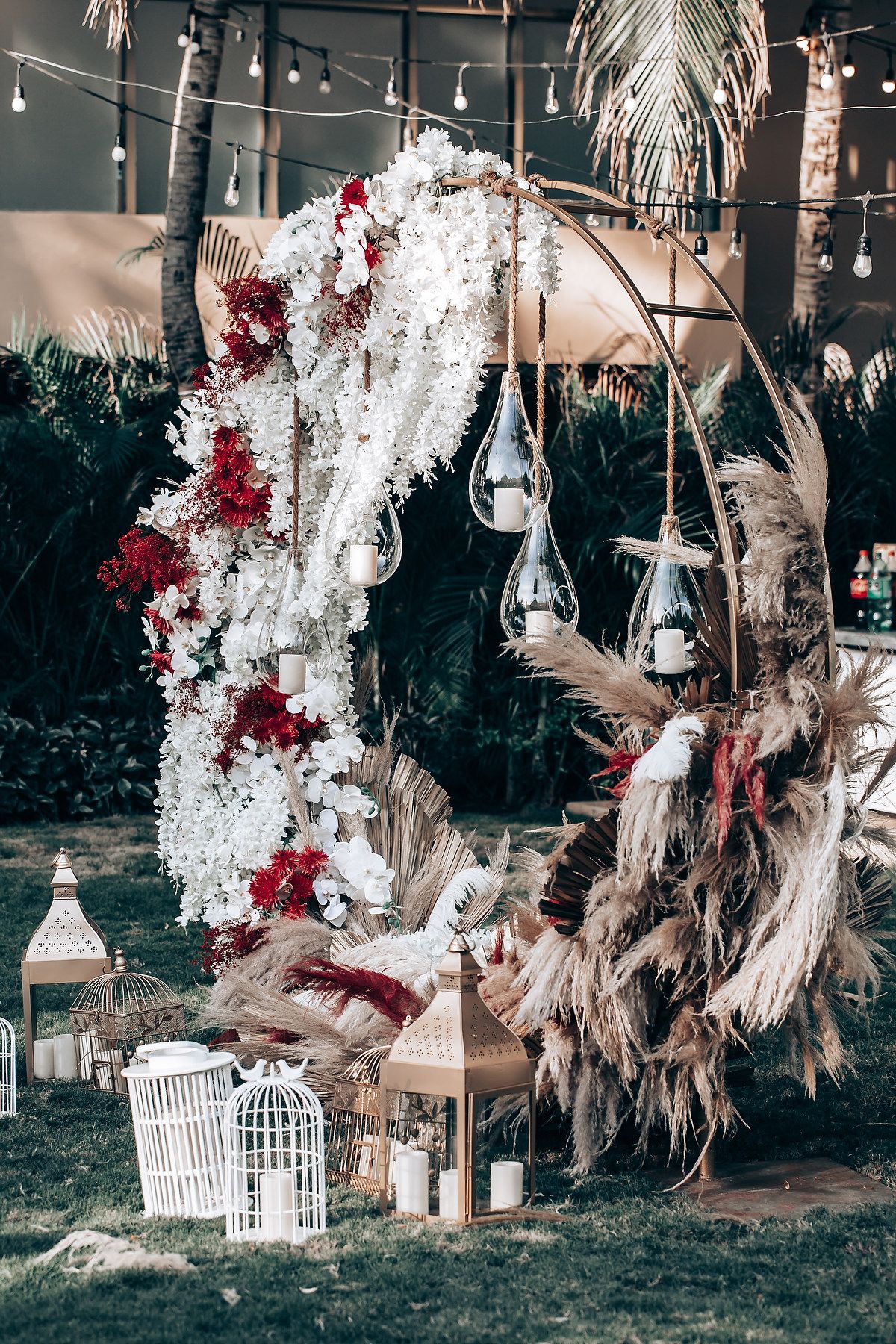 Decorative white birdcages and dried pampas grass arrangements with red floral accents create an elegant outdoor setting.