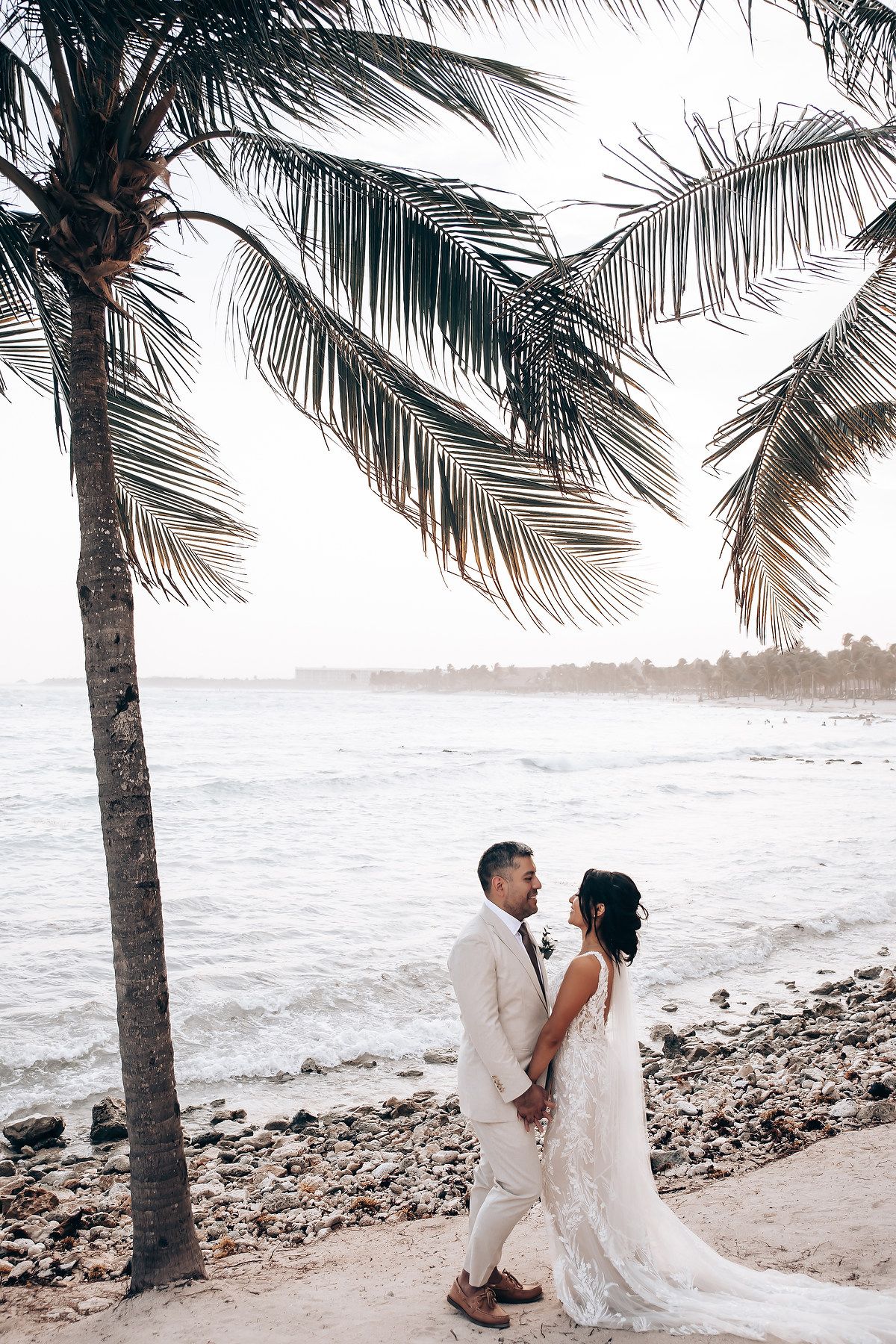 Couple shares intimate moment under swaying palm trees on a rocky tropical beach.