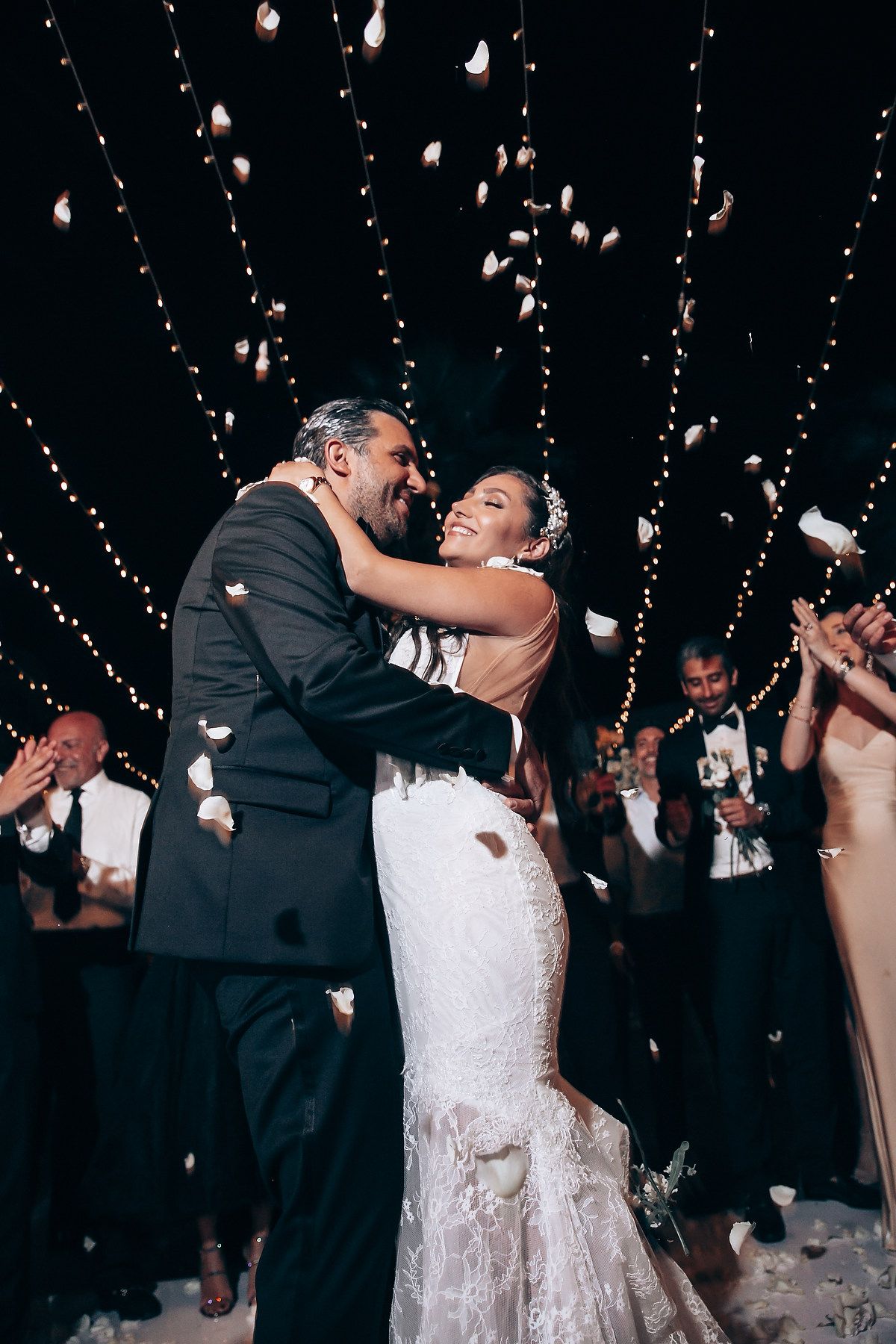 Wedding celebration with falling rose petals under romantic string lights.