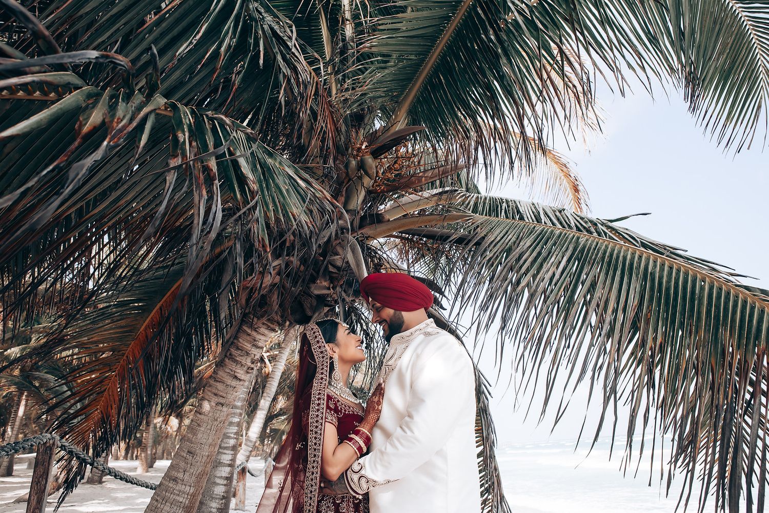 Palm fronds frame an outdoor beach wedding setup with white decor.
