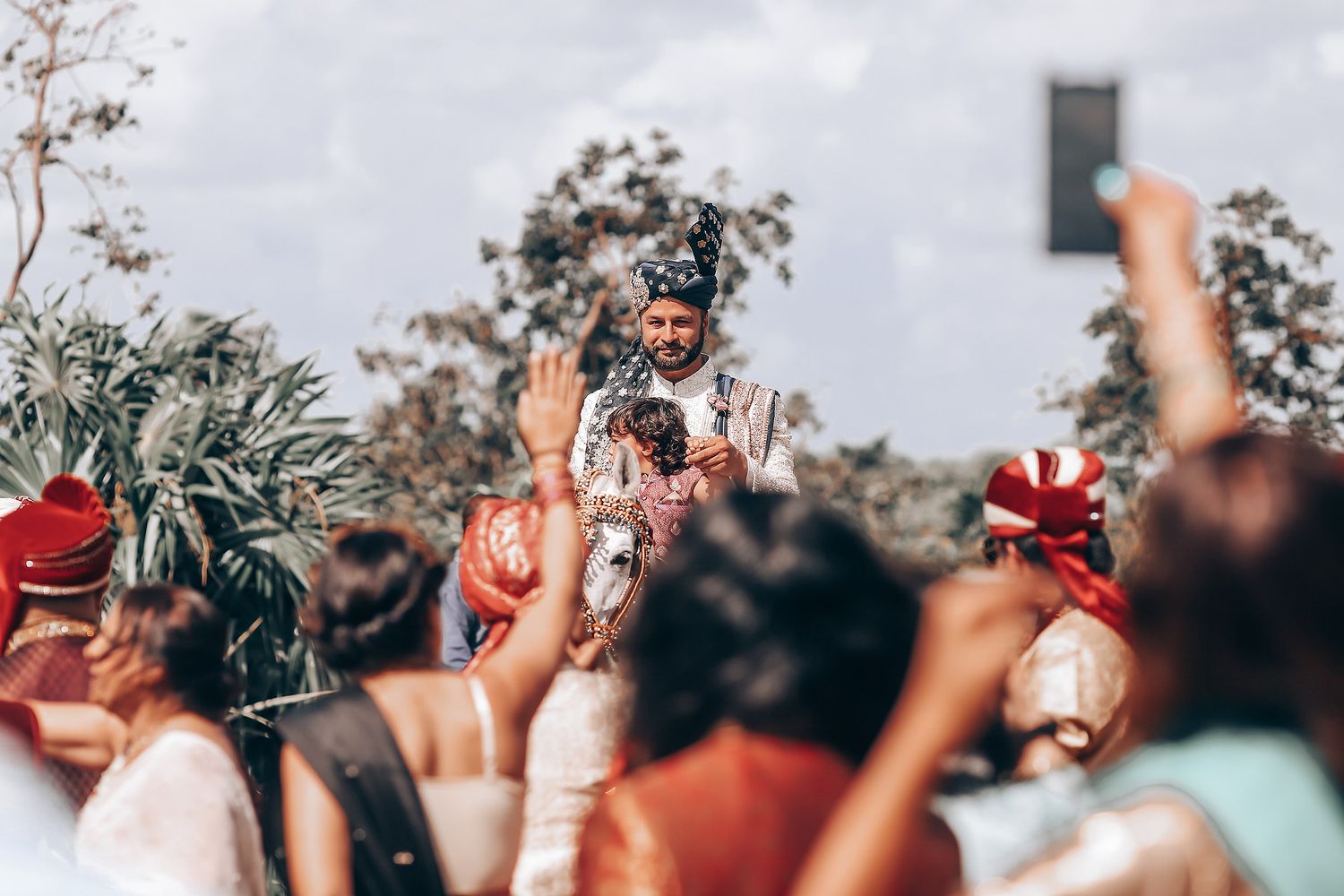 A crowd of concert-goers raise their hands and phones in the air during an outdoor music festival performance.