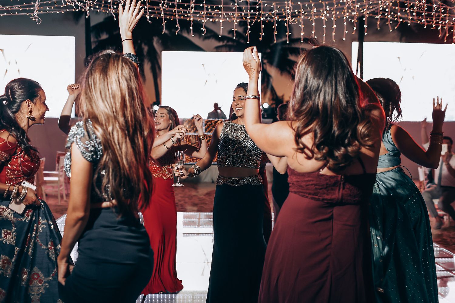 Wedding reception guests dancing under string lights and decorations at an indoor venue.