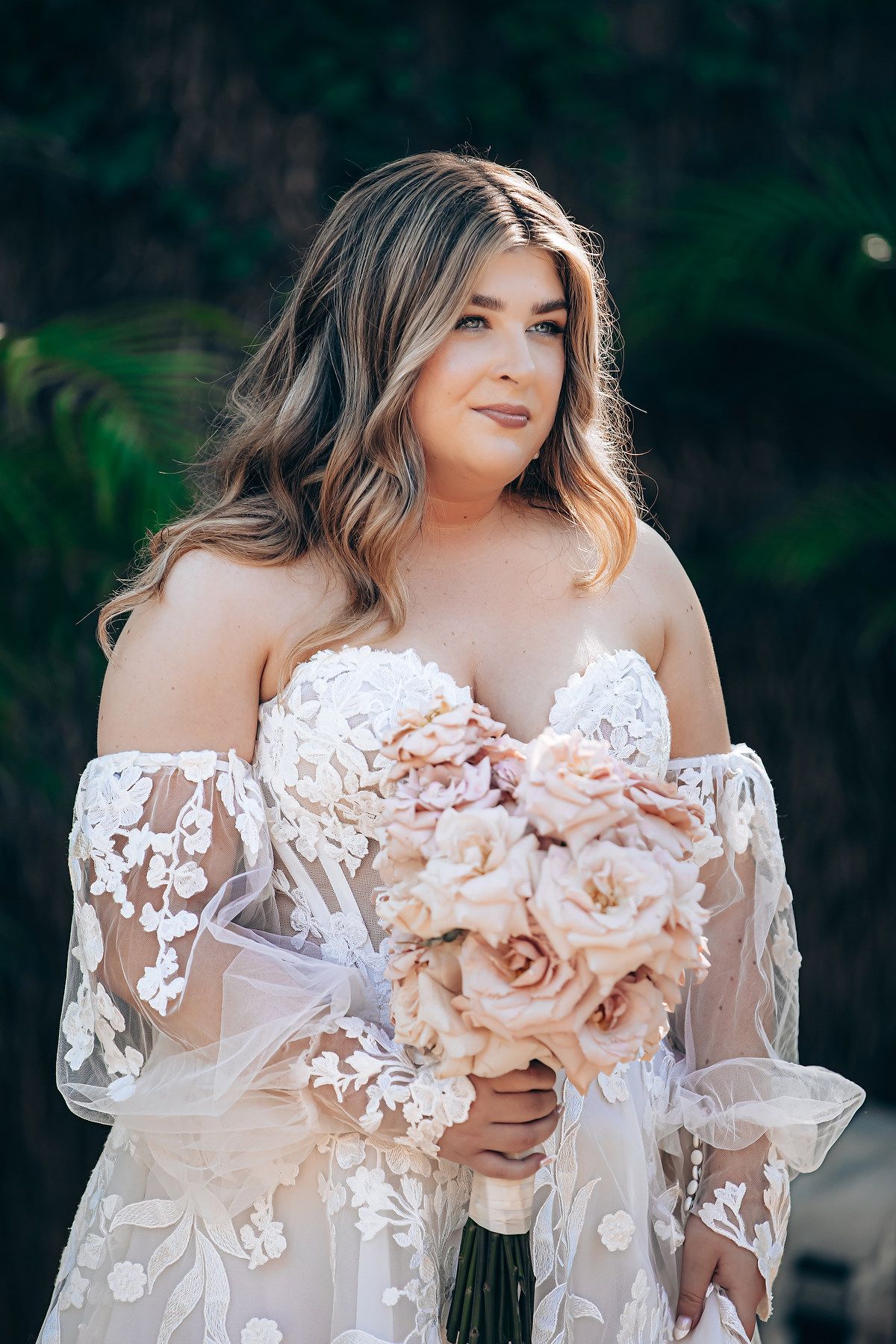 Elegant lace wedding dress with sheer sleeves and blush pink bouquet details.