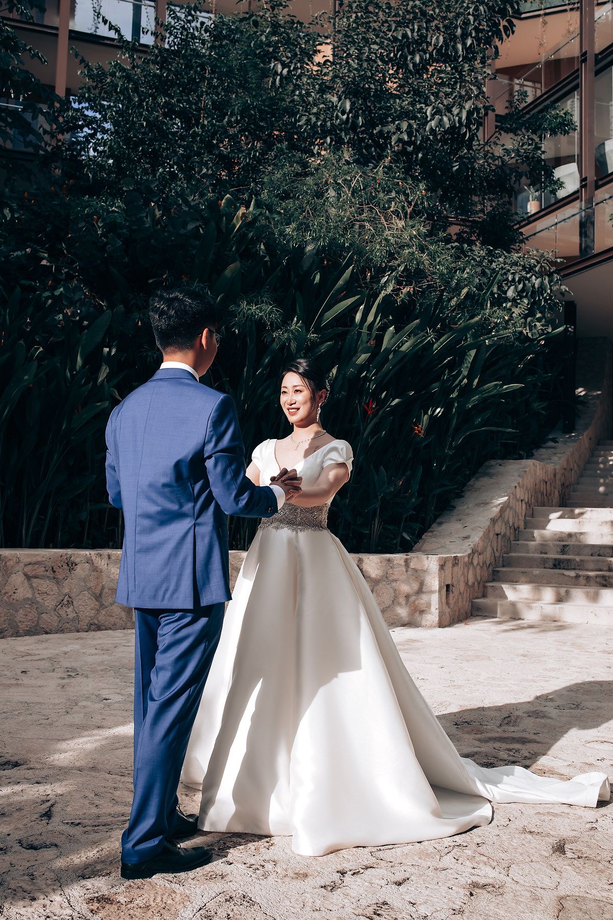 Couple in wedding attire sharing a moment on stone pathway surrounded by greenery.