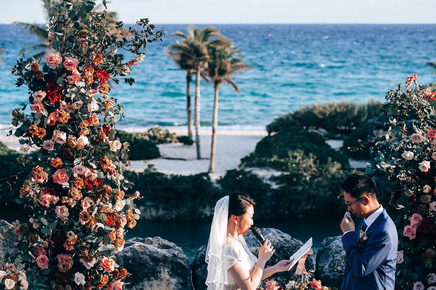 Oceanfront wedding ceremony setup with floral arrangements and blue water backdrop.