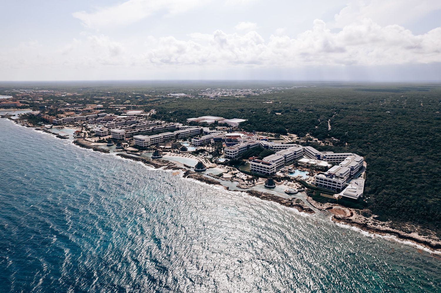 Aerial panoramic view of coastal buildings and infrastructure along the ocean shoreline on a sunny day.