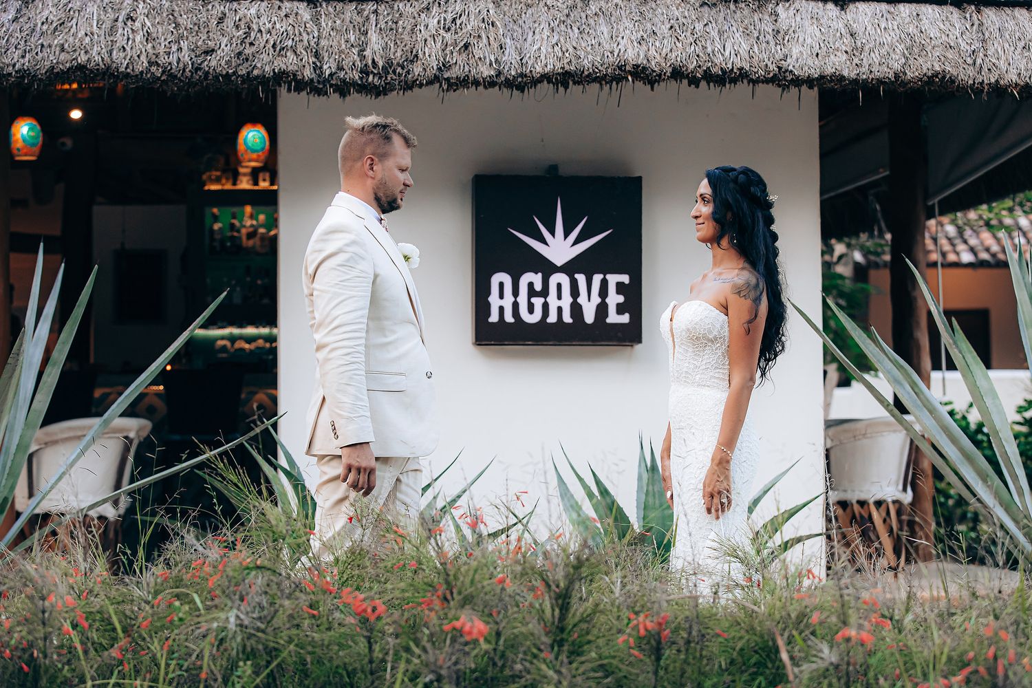 Wedding couple walking along thatched-roof tropical venue pathway.