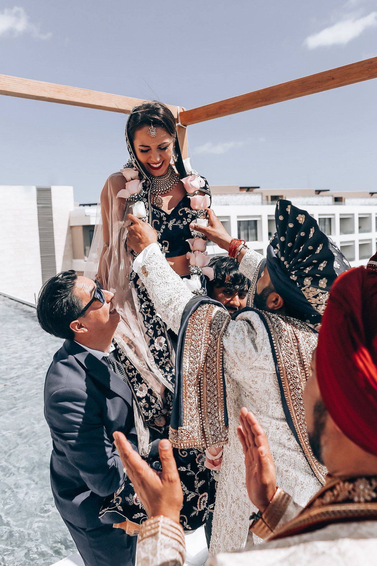 Wedding celebration showing guests lifting someone in traditional attire during outdoor ceremony.