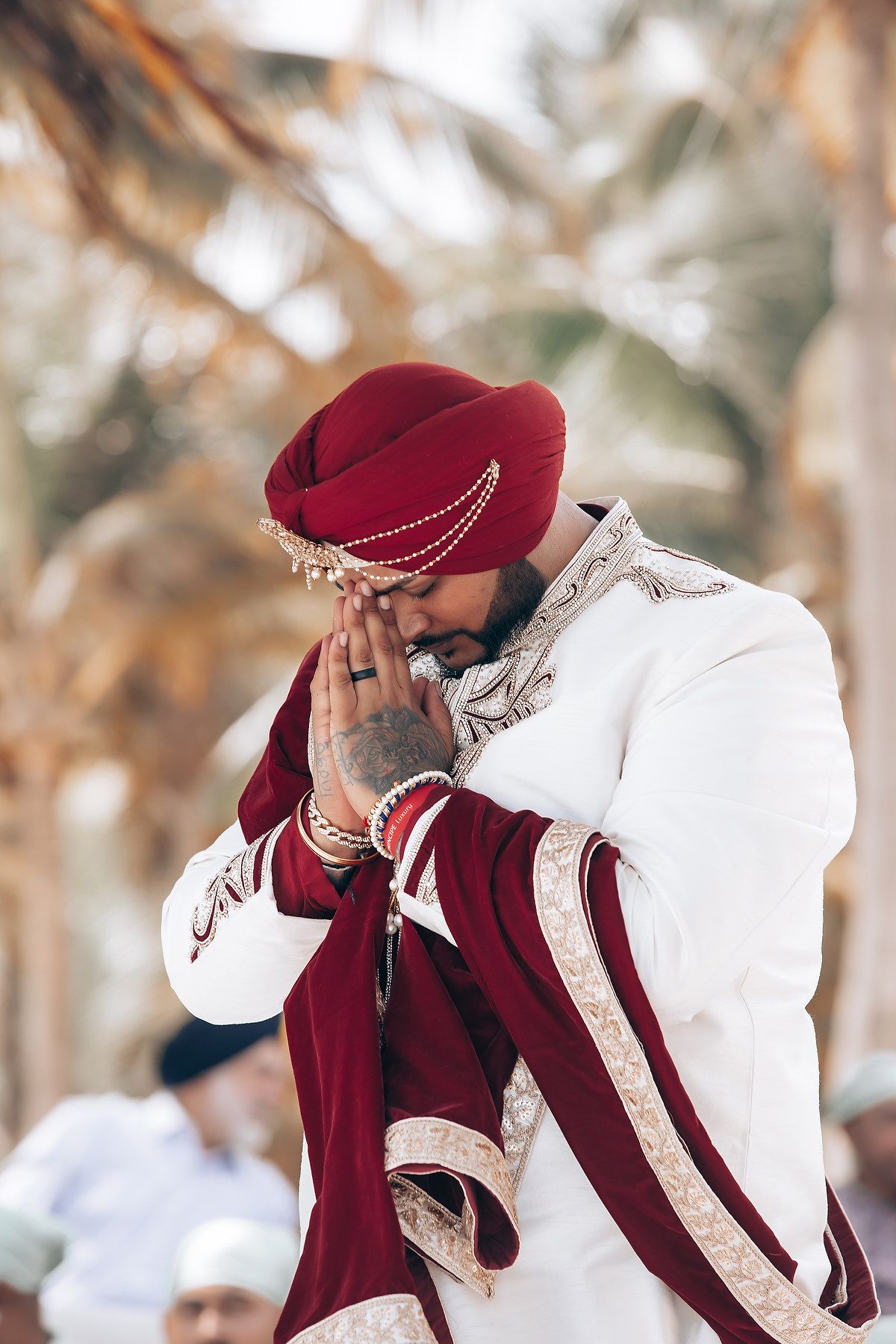 Wedding ceremony participant in burgundy and white traditional attire during emotional moment.