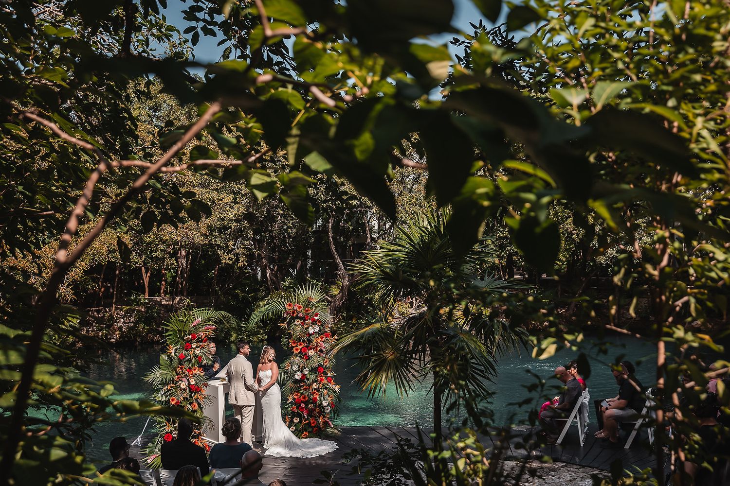Tropical garden wedding ceremony framed by lush foliage and red floral arrangements.