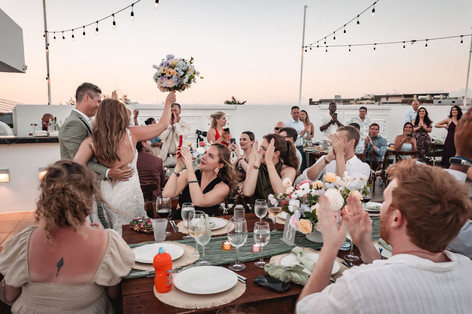 Reception tables decorated with string lights overlooking the ocean at dusk.