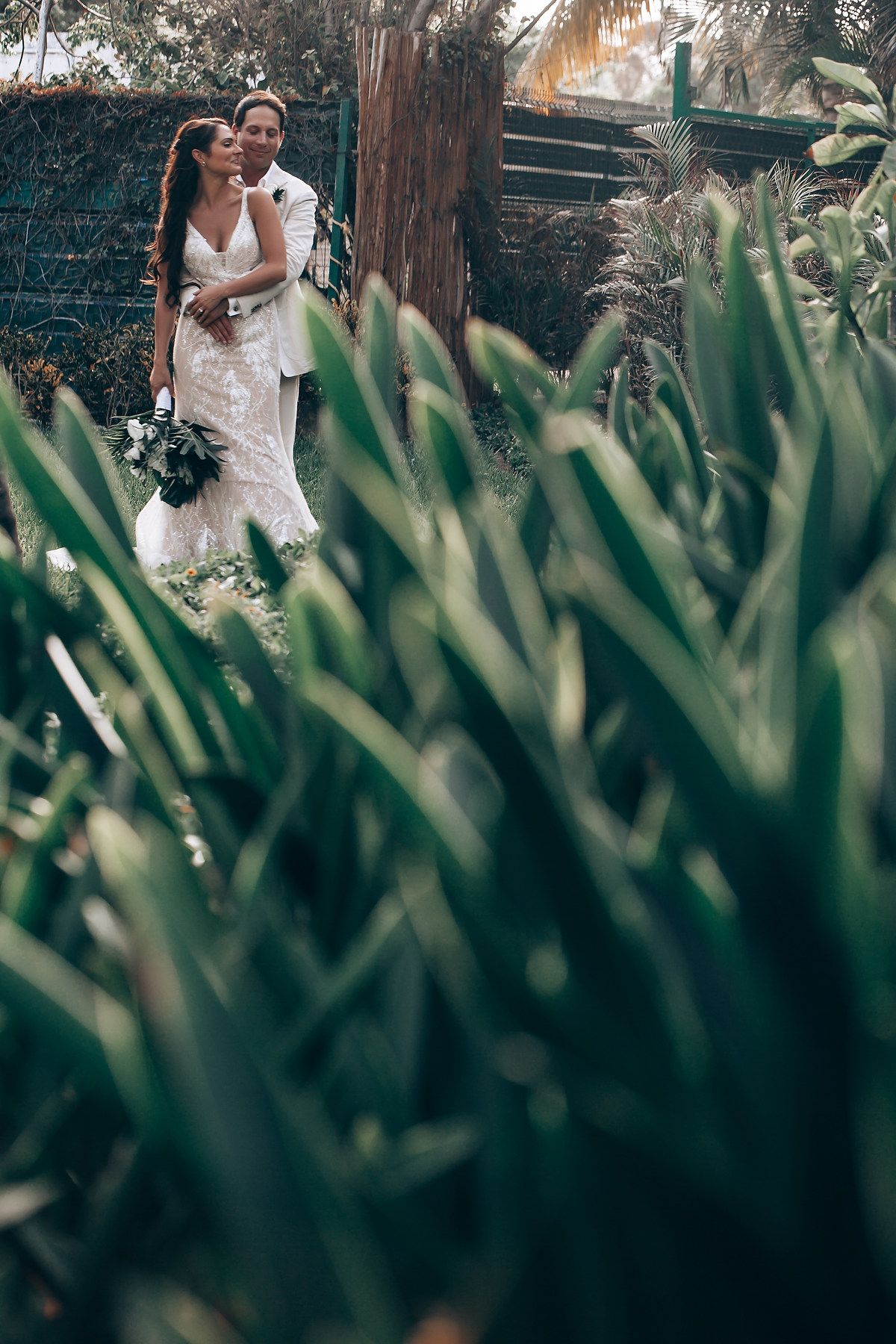 Romantic garden wedding photos with tropical plants in the foreground.